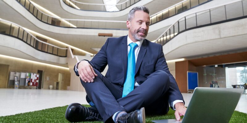 Businesssman sitting on synthetic turf using laptop