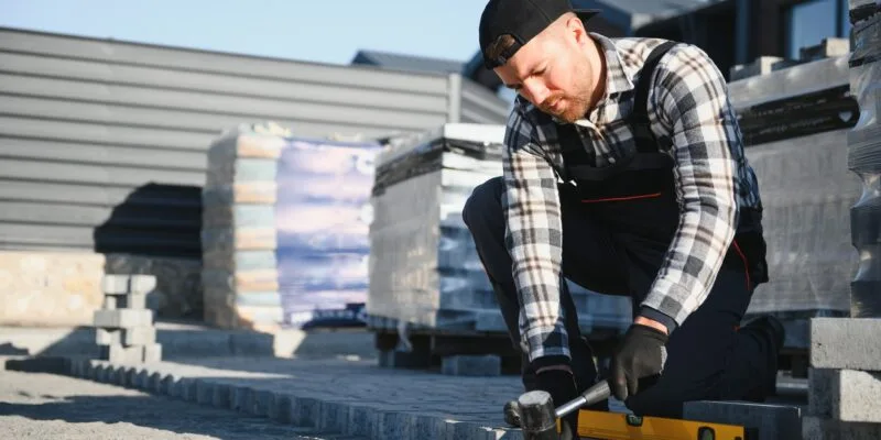 Landscaping paver worker laying paving stones on sandy ground of construction patio yard site
