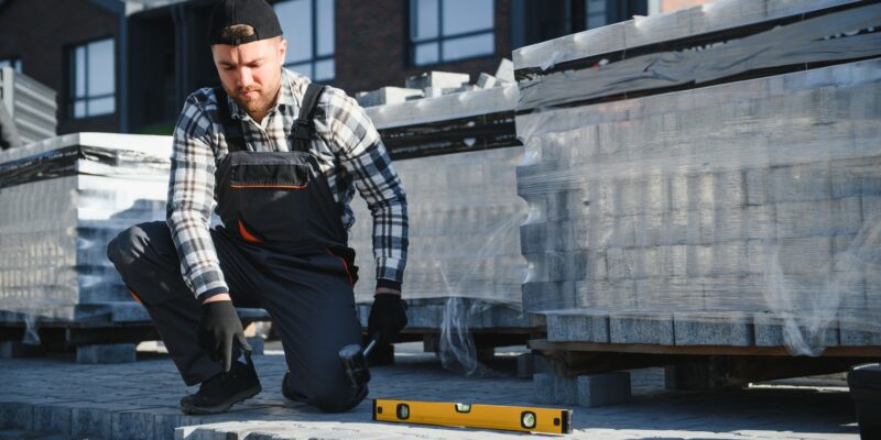 Landscaping paver worker laying paving stones on sandy ground of construction patio yard site