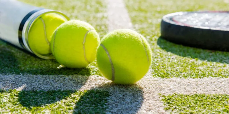 Paddle tennis racket and balls on artificial turf, showcasing vibrant green surface ideal for sports activities.